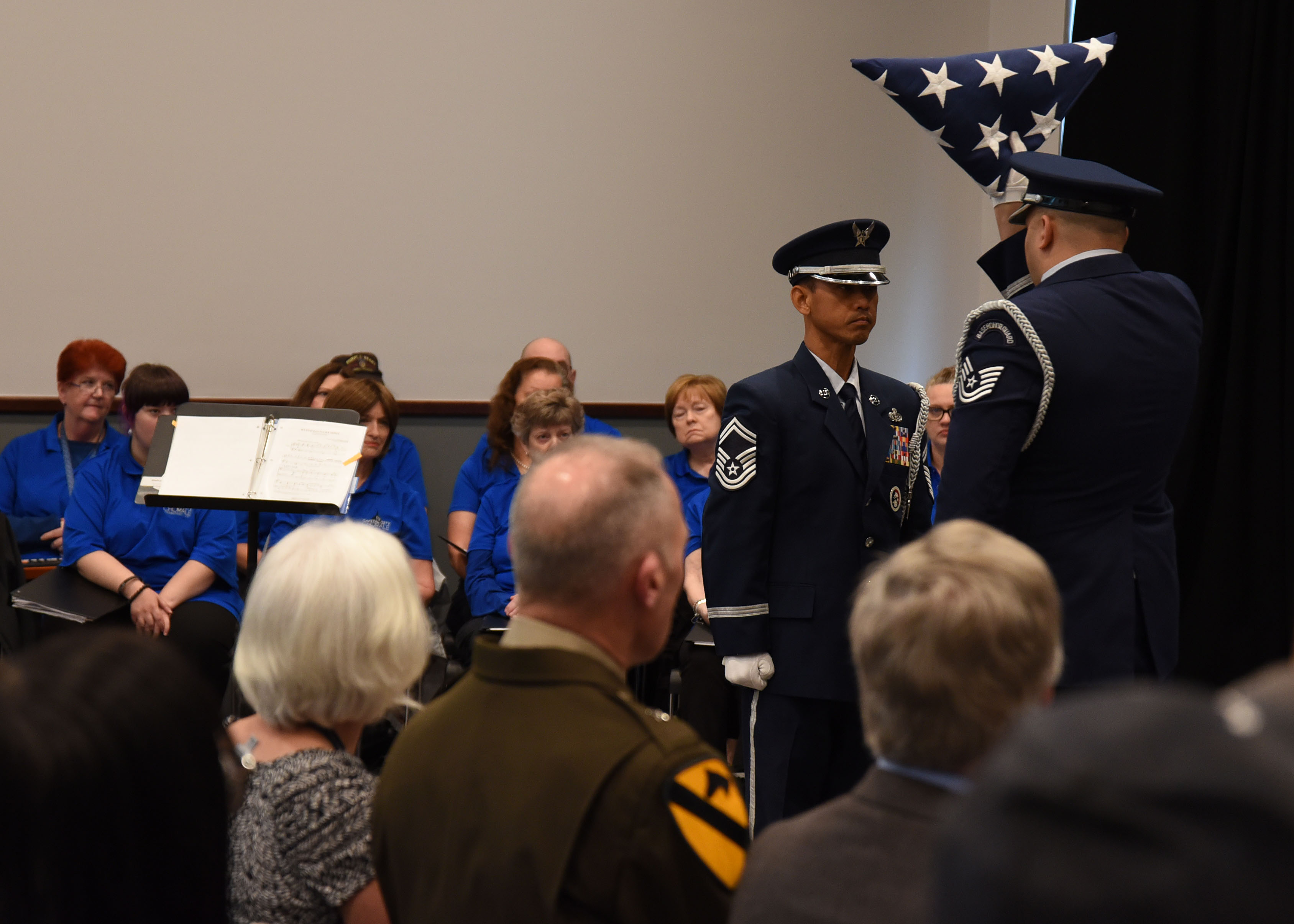 Two uniformed men finish folding an American flag in front of a crowd to display reverence.