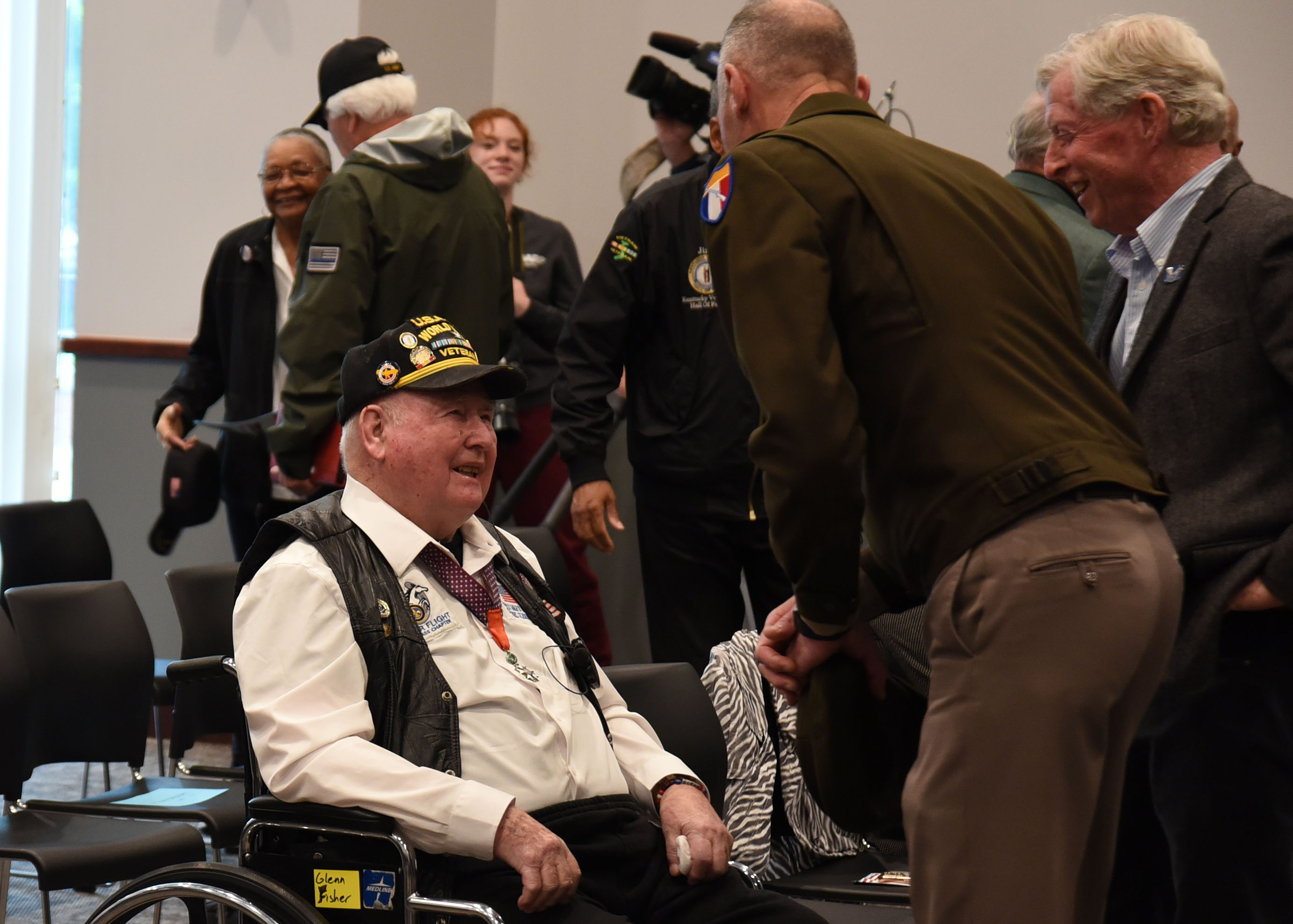 A world war two veteran in a wheelchair speaks with a couple event attendees.