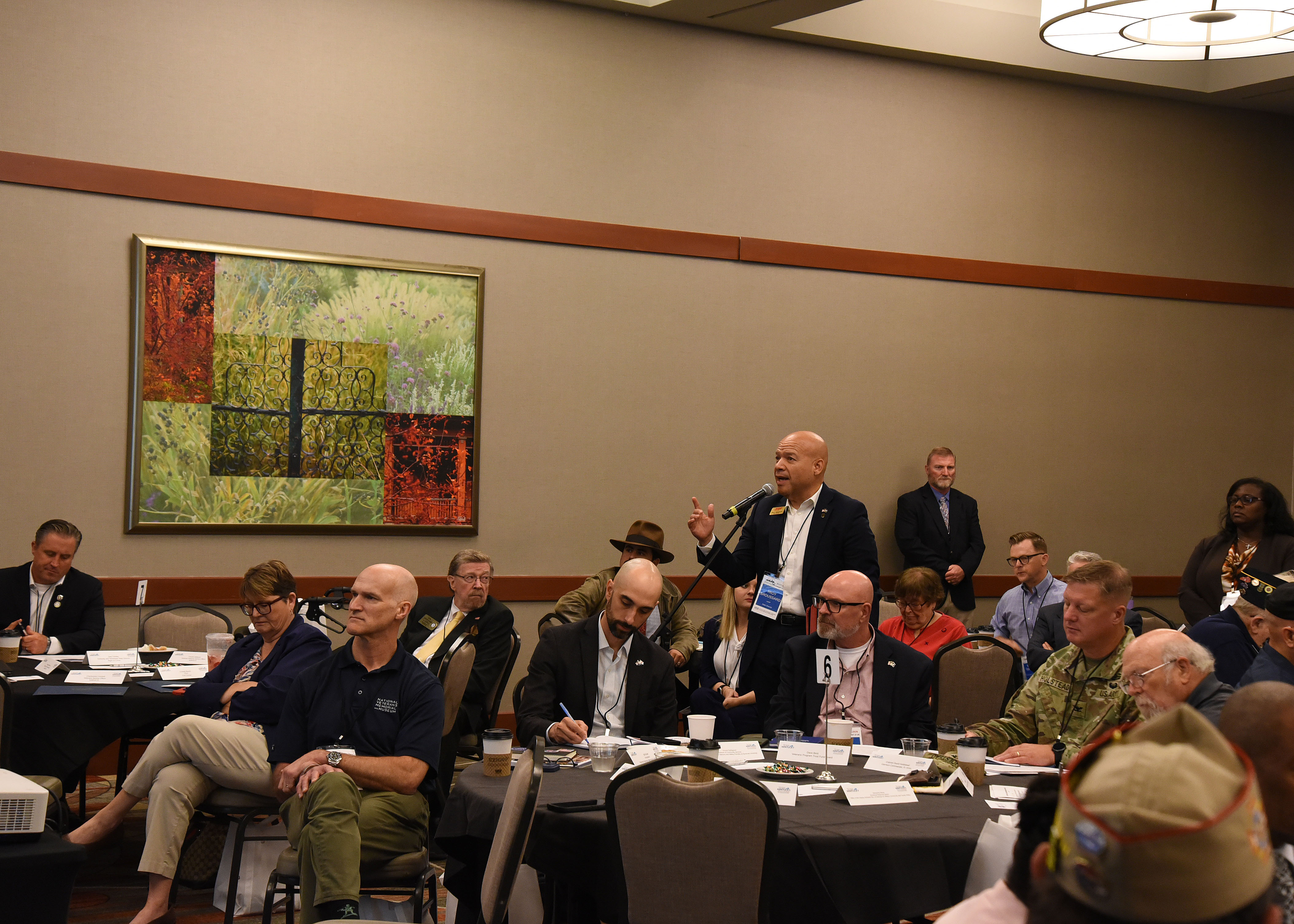 A man stands amongst tables at a microphone to ask questions.