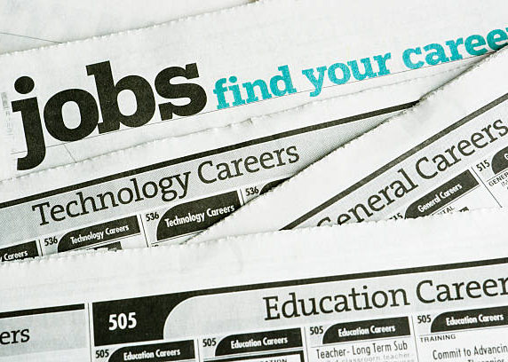 Newspaper job listing pages, stacked to illustrate job search and employment opportunities and the job hunting process of looking for careers and occupations in the classified ad section of printed papers. 