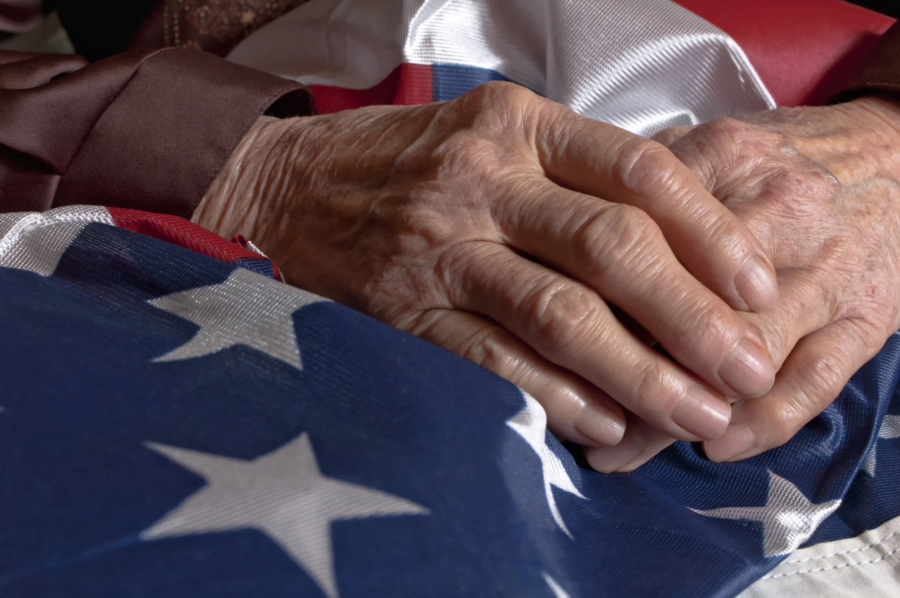 Picture of Older Veterans Hands resting on American Flag.  