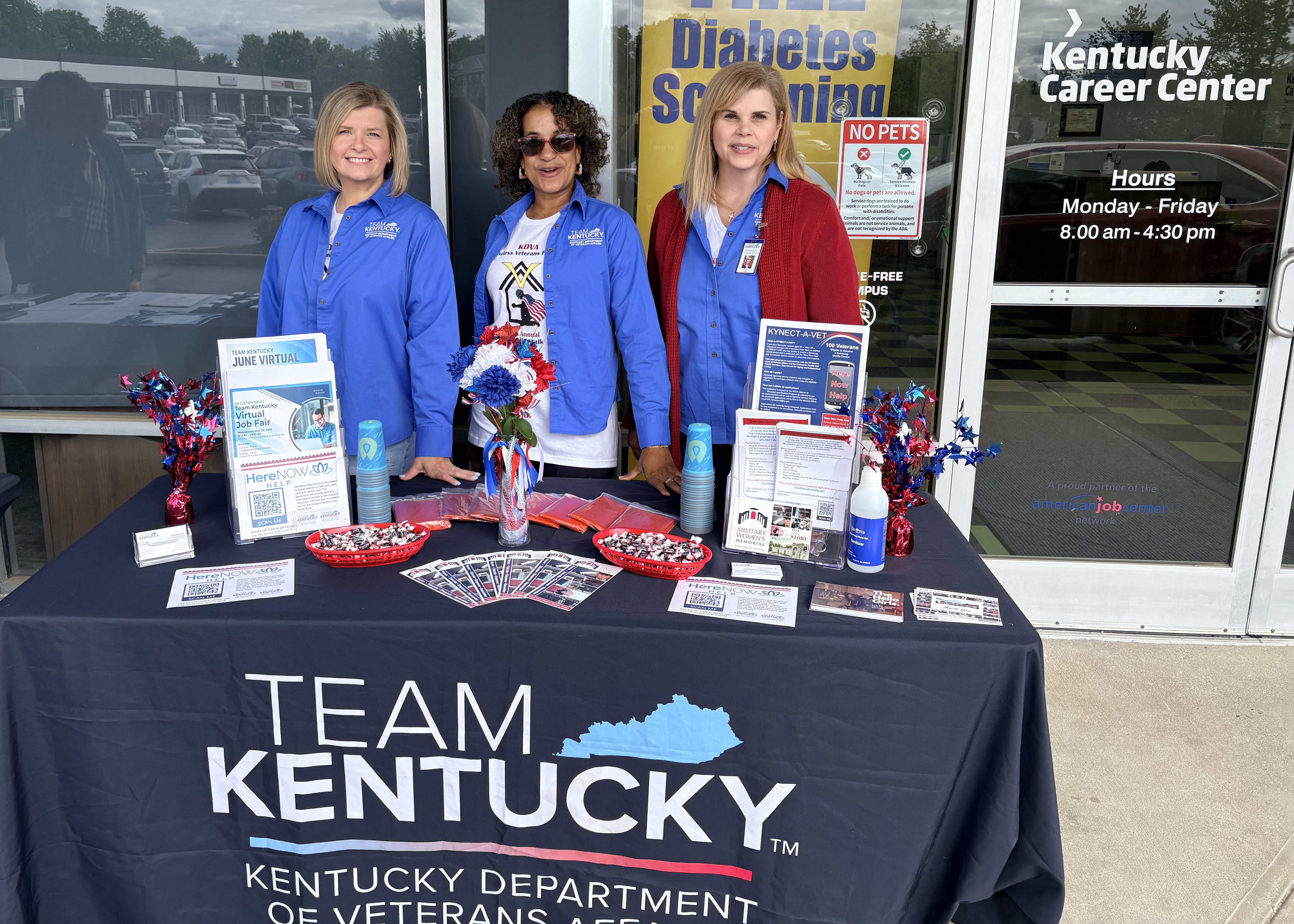 Picture of 3 women in blue shirts standing behind a table booth.